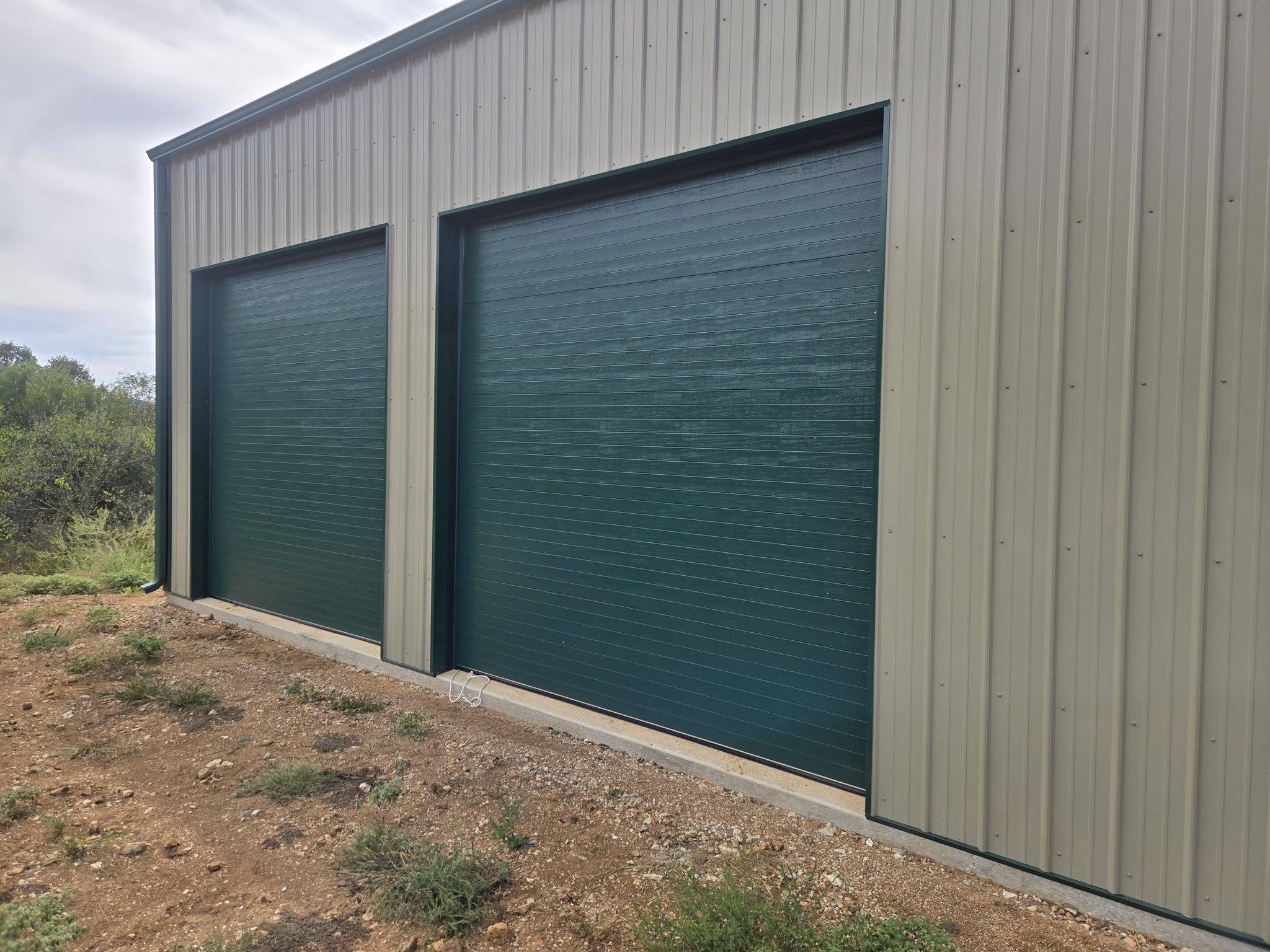 Two green commercial overhead doors installed on a metal building